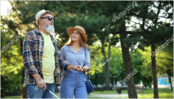 Picture of a young lady helping a blind man walk the street.